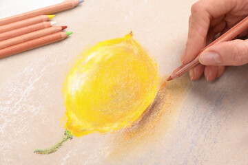 Wall Mural - Woman drawing lemon on paper with pastel pencil at table, closeup