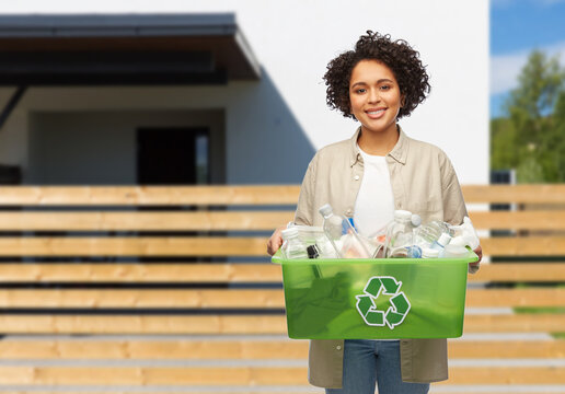 waste sorting and sustainability concept - smiling young african american woman holding plastic box with trash over living house background