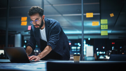 Wall Mural - Successful Handsome Creative Director Working on Laptop Computer in Big City Office Late in the Evening. Businessman Preparing for a Marketing Plan in Conference Room.