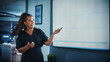 © Gorodenkoff - Company Operations Director Holds Sales Meeting Presentation for Employees and Executives. Creative Black Female Uses TV Screen with Growth Analysis, Charts, Ad Revenue. Work in Business Office.