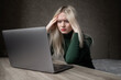 © Екатерина Бучинская - A sad and very tired blonde woman in a green golf is bored working at home with a laptop. Girl sitting at the table in a bad mood in the room. Online learning. Unsightly video conference. High quality