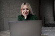 © Екатерина Бучинская - Emotional cheerful blonde girl in green golf is talking via video link at an online conference. Works at home with a laptop. Sits at the table in a positive mood in the room. Online learning. High