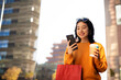 © Jelena - Pretty chinese girl using mobile phone and holding coffee to go. Beautiful woman enjog in coffee while walking on the city street..