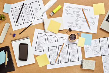 Wall Mural - top view image of busy web ux designers workspace with many mobile app wireframe sketches and user f