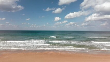 Wall Mural - Waves breaking on a clear sandy beach with cloudy blue sky in the background.
