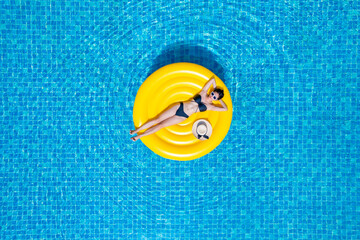 Top view of young asian woman in bikini on the yellow inflatable ring in the pool at private villa. Summer holliday concept