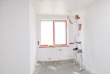 Painter Worker On Stilts With Roller Painting Ceiling Into White