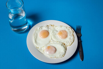 Canvas Print - Fried eggs on a blue background. Three fried eggs on a plate. Quick and tasty breakfast