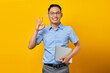 © Bangun Stock Photo - Portrait of smiling handsome Asian man in glasses holding laptop and gesturing okay sign isolated on yellow background. businessman and entrepreneur concept
