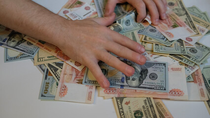 Close-up of male hands raking and pulling a bunch of money from Russian five thousandth bills and American dollars. Greed, bribery and corruption