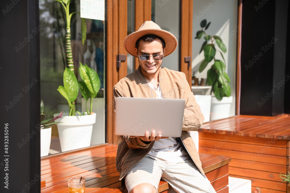 Stylish young man using laptop in street cafe