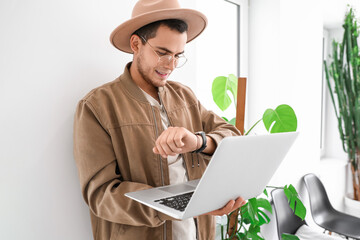 Poster - Young man with laptop looking at wristwatch in cafe