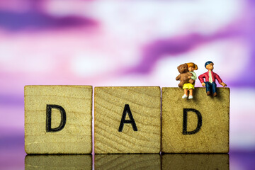 Father's day Concept. Two children sitting on dad letters magenta sky backdrop. Miniature people. Macro