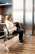 © dark_blade - Traveler woman wearing face mask at the airport. Young caucasian woman sitting at the airport using smartphone