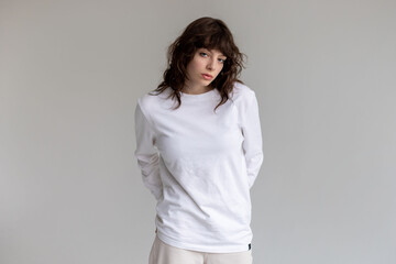 Young woman with curly hair in a white long sleeve t-shirt stands on a white background. Mock-up.