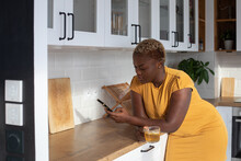 Black Woman Using Smartphone In The Kitchen