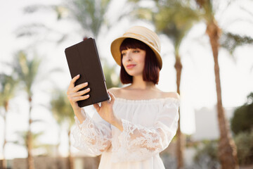 Attractive young woman tourist speaking using tablet, always-on connection. Videochat with friends or relatives, reading news on the Internet using wifi in exotic hotel during summer vacation.