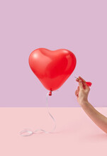 Woman piercing heart balloon with needle