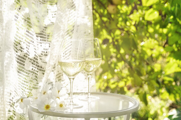 Beautiful glasses of white wine with white flowers on glass table in summer garden in sunlight. Copy space. Summer drinks concept.