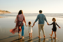 Family Strolling On Beach At Sunset