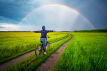 Woman With Hoodie On A Bike Opens Her Arms By The Gravel Road. Beautiful Rain Bow Over The Forest.