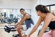 © Ivan Gener/Stocksy - Laughing friends exercising on gym bikes