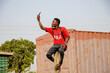 © Finest Imagery  - African man sitting on a concrete pillar with his phone raised in search for mobile network.