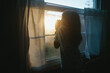 © Maria Manco/Stocksy - Young girls looks out window with sun setting outside