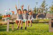 © CSRRDRGZ - Hermanos amigos niños felices disfrutando y jugando levantando las manos combinados vestidos igual divertidos alegres sentados en una banca en parque infantil al aire libre