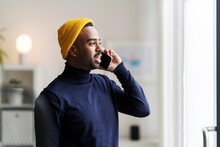 Modern Man In Bright Hat Talking On Smartphone At Home