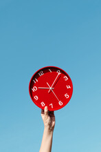 Man Holding A Red Clock Against The Sky