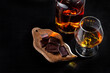 © 02irina - A glass of cognac, cognac in a bottle and pieces of chocolate on a dark background. Copy space