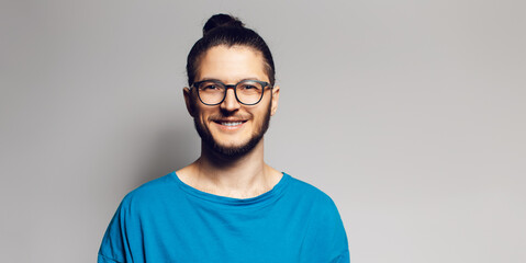 Studio portrait of young smiling man in blue shirt on grey background.