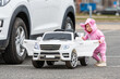 © ako-photography - a little girl at a big white childrens electric toy car in the parking lot next to a real car