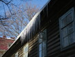 Icicles in the rays of the sun on the roof of a wooden house against the blue sky close-up. Open window in the old window of an old wooden house.