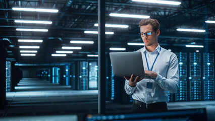 Fototapete - Caucasian Young Male IT Specialist Using Laptop, Standing in Data Center. Skilful Man Works on Web Services. Cloud Computing, Server Analytics, Cyber Security Maintenance