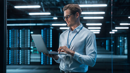 Poster - European Male IT Specialist Using Laptop Computer, Standing in Big Warehouse Data Center. System Administrator working with SAAS. E-Business Digital Entrepreneur Examining Cloud Web Services