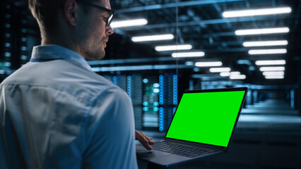 Wall Mural - View Over the Shoulder of Male IT Specialist Using Laptop Computer in Data Center, Looking at the Screen. Successful Businessman and e-Business Entrepreneur Working Alone. Innovation Concept