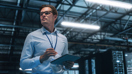 Wall Mural - Handsome IT Specialist Using Tablet Computer in Data Center, Looking at the Screen. Succesful Businessman and e-Business Entrepreneur Overlooking Server Farm Cloud Computing Facility.