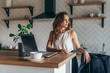 © undrey - Portrait of woman in the kitchen at the table with a laptop