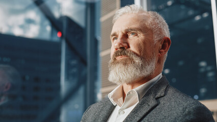 Wall Mural - Portrait of Successful Middle Aged Businessman in a Suit Riding Glass Elevator to Office in Modern Business Center. Male Looking at Modern Downtown Skyscrapers Out of the Panorama Window in the Lift.