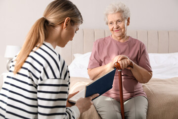 Poster - Young caregiver reading book to senior woman in bedroom. Home care service