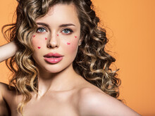 Portrait Of A Beautiful Girl With Painted Red Hearts On Her Face. Fashion Photography. Sexy Blonde With Curly Hair. An Expressive And Sensual Model With Bright Makeup Poses In The Studio.