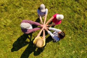 Canvas Print - Top aerial view of people holding hands together in circle on green grass. Drone photography