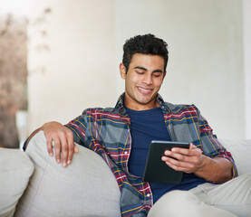 Canvas Print - Staying connected to the world. Shot of a handsome young man using his tablet while relaxing on the sofa at home.