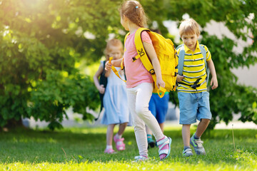 Wall Mural - Cute children with rucksacks walking in the park near the school