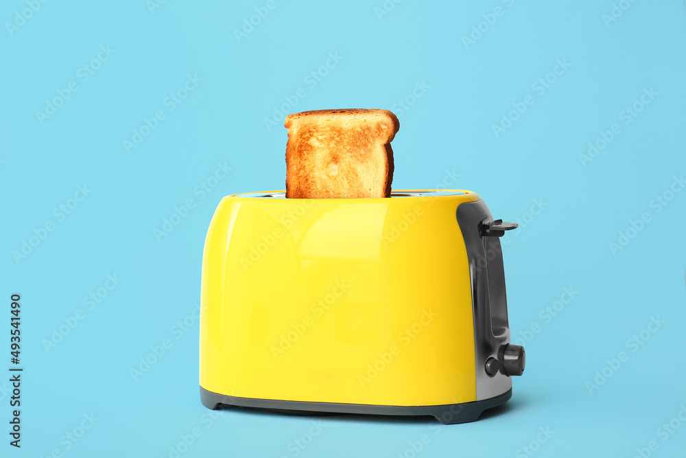 Modern toaster with bread slice on blue background