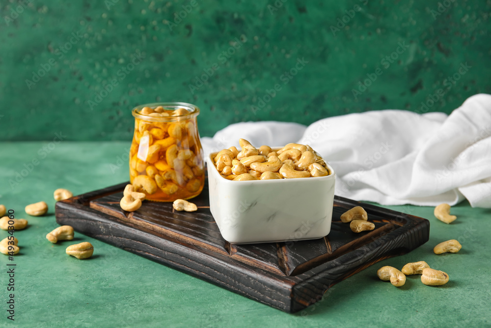 Board with sweet cashew nuts in honey on color background