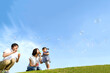 青空を背景にシャボン玉で遊ぶ若い夫婦と幼い娘。家族,親子,幸せ,愛情,育児のイメージ