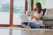 © interstid - Happy Asian woman laughing while talking on smartphone and using laptop at home